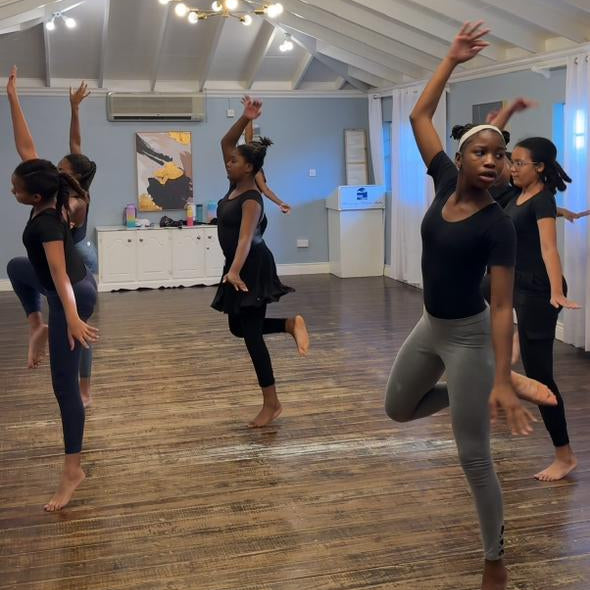Group of dancers practicing in a studio with wooden floors and white walls.